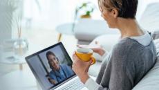 Person sitting on a couch with a laptop on their lap speaking with a healthcare professional virtually